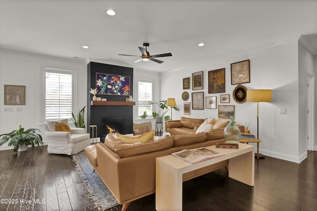 living area with dark wood-style flooring, ornamental molding, a large fireplace, and recessed lighting
