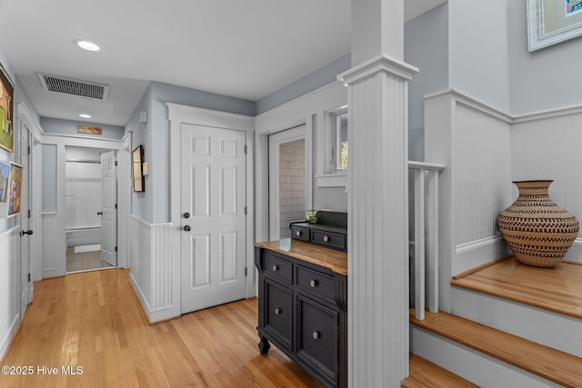 corridor with light wood-style flooring, wainscoting, and decorative columns