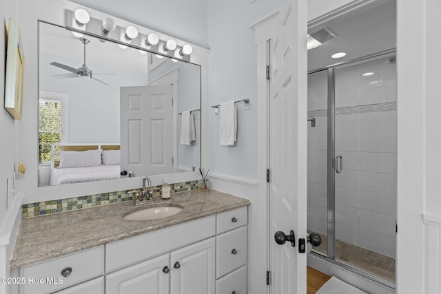 ensuite bathroom with a ceiling fan, a shower stall, vanity, and wainscoting