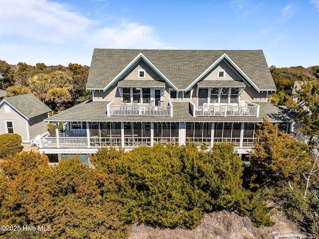 rear view of house featuring roof with shingles, a balcony, and a sunroom
