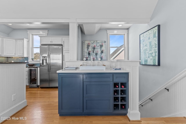 kitchen featuring stainless steel fridge with ice dispenser, beverage cooler, white cabinets, a wainscoted wall, and light wood finished floors