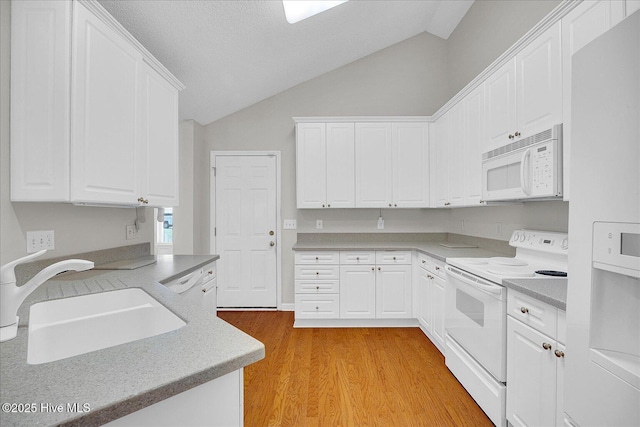 kitchen featuring white cabinets, a sink, white appliances, lofted ceiling, and light wood-type flooring