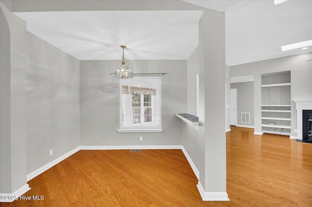 spare room featuring an inviting chandelier, built in features, a fireplace with flush hearth, wood finished floors, and visible vents