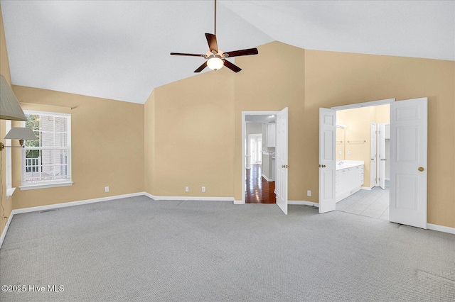 interior space with carpet floors, baseboards, ensuite bathroom, ceiling fan, and high vaulted ceiling