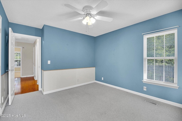 carpeted spare room featuring visible vents, attic access, a textured ceiling, and a ceiling fan