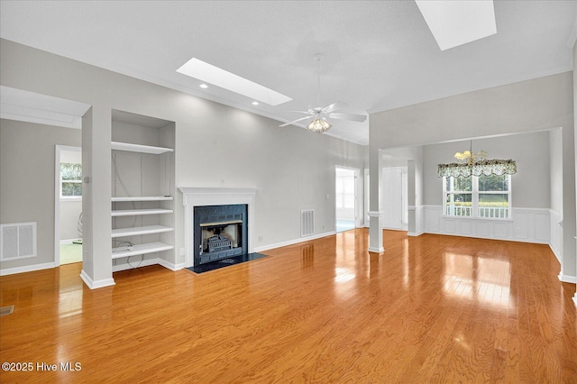 unfurnished living room featuring built in features, a fireplace with flush hearth, wood finished floors, a skylight, and visible vents