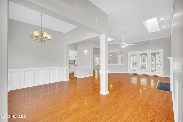 unfurnished living room featuring ornamental molding, arched walkways, light wood finished floors, ceiling fan with notable chandelier, and a skylight