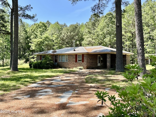 ranch-style home featuring dirt driveway, a chimney, a wooded view, and brick siding