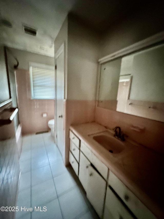 full bathroom featuring tile walls, tile patterned flooring, wainscoting, vanity, and toilet