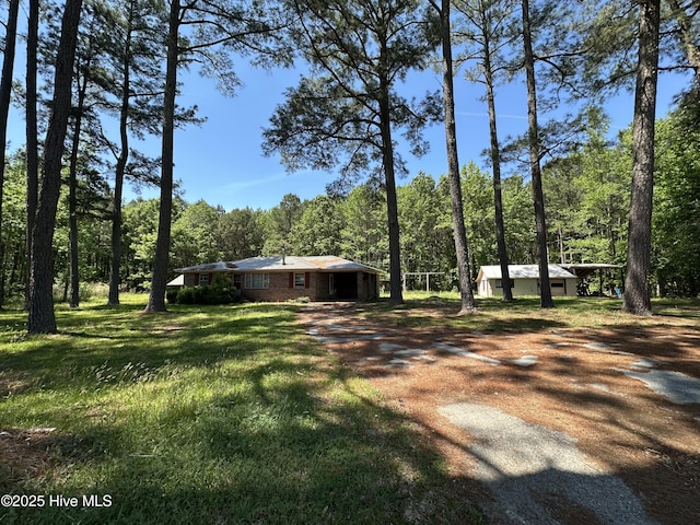 view of yard featuring a carport, a wooded view, and dirt driveway