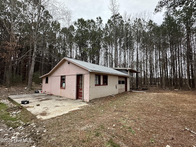 view of home's exterior featuring a view of trees, metal roof, a patio area, and concrete block siding