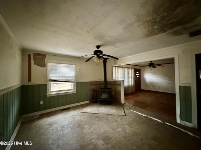 unfurnished living room featuring plenty of natural light, a wood stove, and ceiling fan