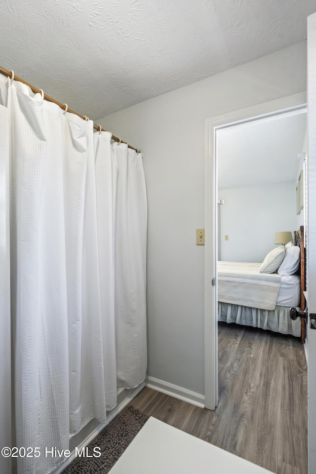 ensuite bathroom featuring baseboards, a shower with curtain, wood finished floors, and connected bathroom