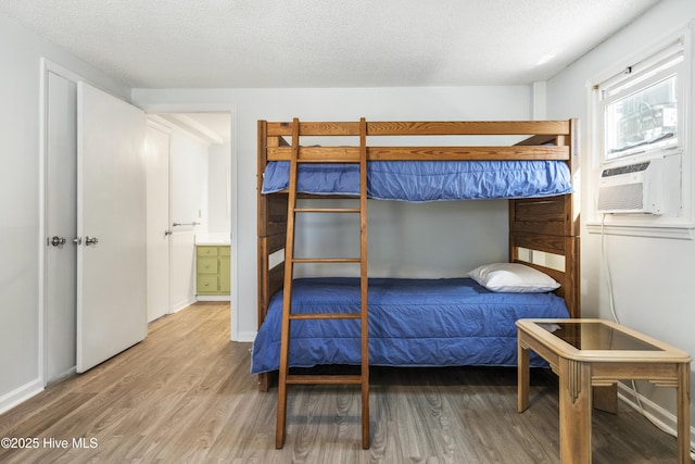 bedroom with a textured ceiling, cooling unit, and wood finished floors