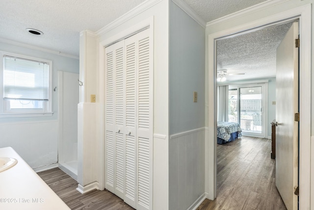 corridor with ornamental molding, a textured ceiling, and wood finished floors