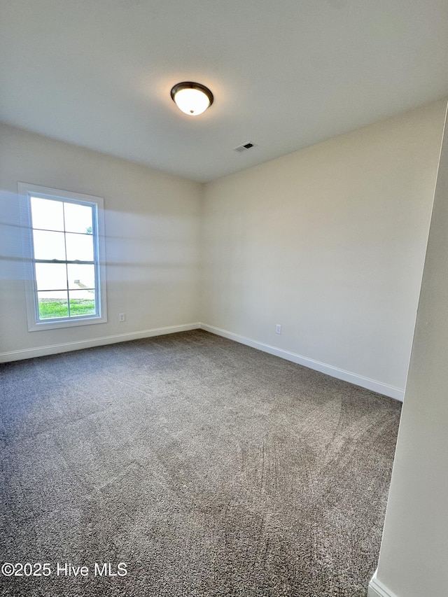 spare room featuring visible vents, baseboards, and dark colored carpet