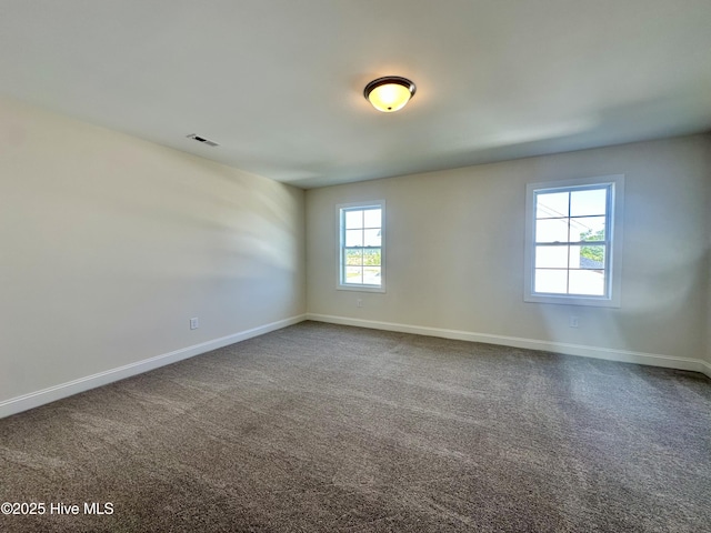 unfurnished room with baseboards, dark colored carpet, and visible vents
