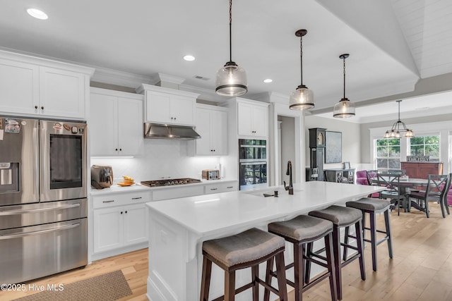 kitchen with a breakfast bar, recessed lighting, under cabinet range hood, a sink, and appliances with stainless steel finishes