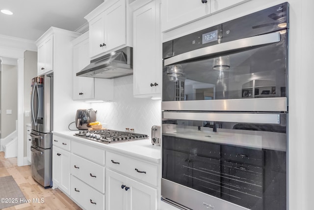 kitchen with light countertops, under cabinet range hood, white cabinets, tasteful backsplash, and appliances with stainless steel finishes
