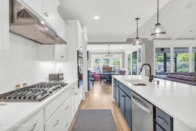 kitchen with a sink, blue cabinetry, stainless steel appliances, open floor plan, and under cabinet range hood