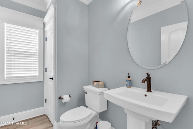 half bath with a sink, toilet, baseboards, wood finished floors, and ornamental molding