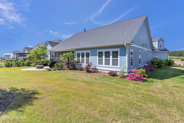 back of property with a lawn, roof with shingles, and an outdoor fire pit