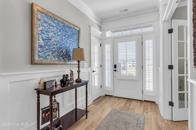 foyer with crown molding, visible vents, and light wood-type flooring