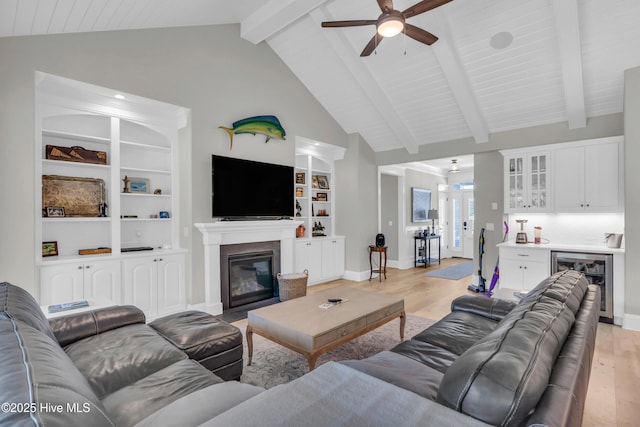 living area featuring a ceiling fan, a bar, a glass covered fireplace, wine cooler, and light wood-style flooring