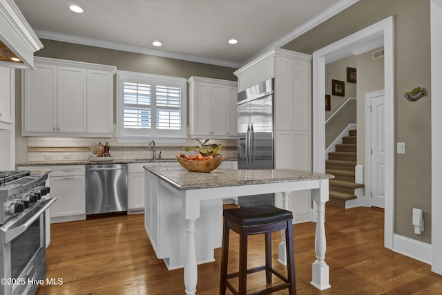 kitchen with stainless steel appliances, a kitchen bar, backsplash, ornamental molding, and white cabinets