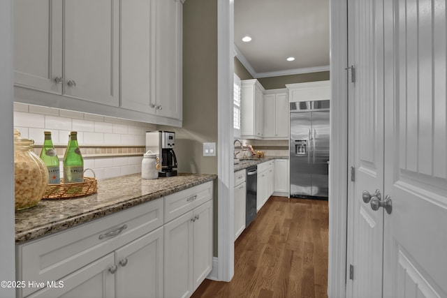kitchen with appliances with stainless steel finishes, backsplash, white cabinets, dark wood-style floors, and ornamental molding