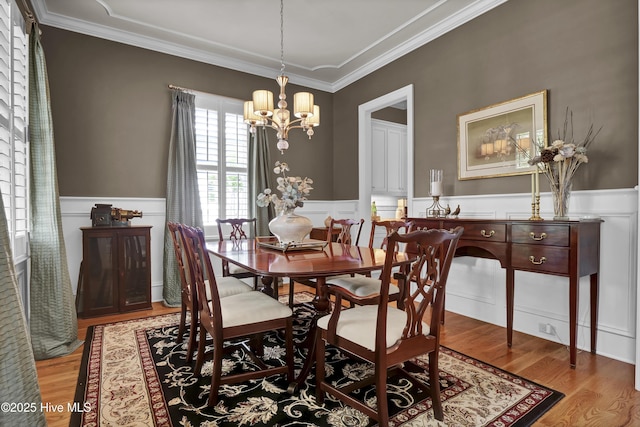 dining area with a wainscoted wall, a chandelier, crown molding, light wood-style flooring, and a decorative wall