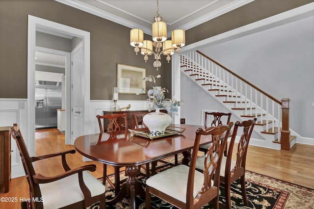 dining room featuring stairway, wood finished floors, crown molding, a wainscoted wall, and a chandelier