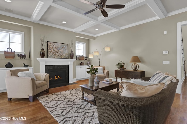 living area featuring coffered ceiling, ceiling fan, a fireplace with flush hearth, wood finished floors, and beamed ceiling