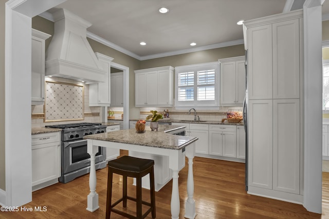 kitchen with stainless steel stove, custom range hood, white cabinetry, backsplash, and ornamental molding