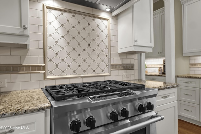kitchen featuring high end stove, tasteful backsplash, white cabinets, and light stone counters
