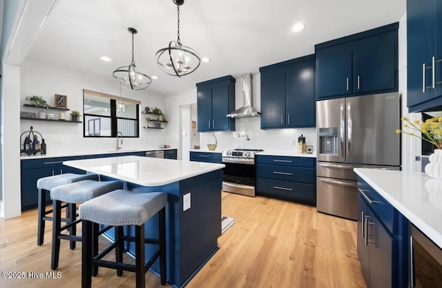 kitchen with open shelves, appliances with stainless steel finishes, a sink, wall chimney exhaust hood, and blue cabinets