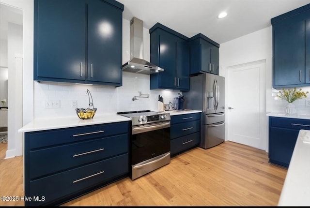 kitchen with blue cabinets, appliances with stainless steel finishes, wall chimney range hood, and light countertops