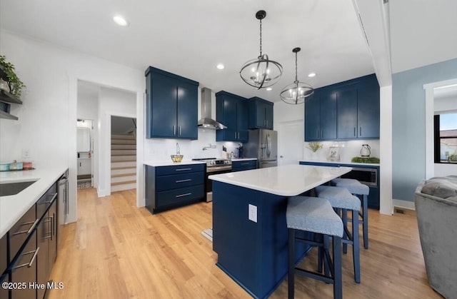 kitchen featuring a breakfast bar area, wall chimney range hood, light countertops, blue cabinets, and appliances with stainless steel finishes