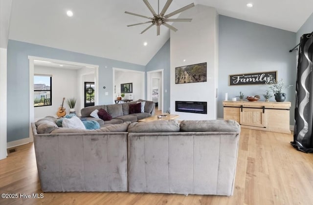 living room featuring a glass covered fireplace, ceiling fan, high vaulted ceiling, recessed lighting, and light wood finished floors