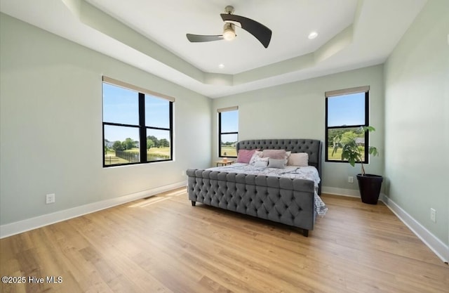 bedroom with a ceiling fan, baseboards, a tray ceiling, recessed lighting, and light wood-style flooring