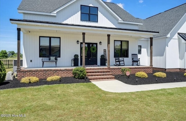exterior space featuring a shingled roof, board and batten siding, covered porch, and a front yard