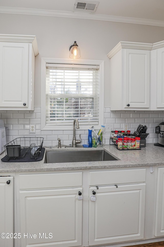 kitchen with a sink, white cabinetry, tasteful backsplash, visible vents, and ornamental molding
