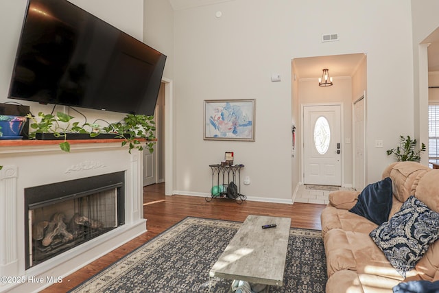 living area featuring baseboards, visible vents, wood finished floors, and a towering ceiling