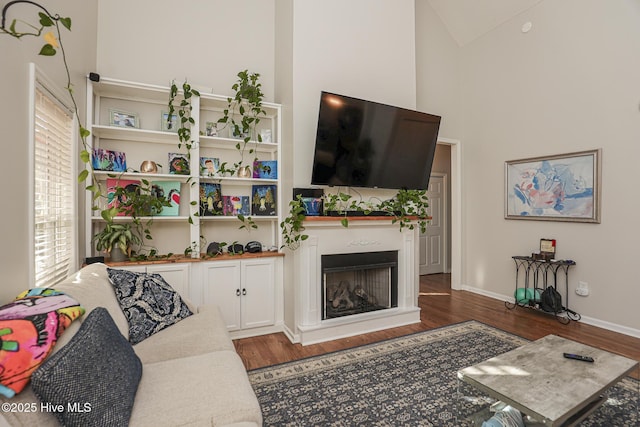 living room featuring high vaulted ceiling, baseboards, a fireplace, and wood finished floors