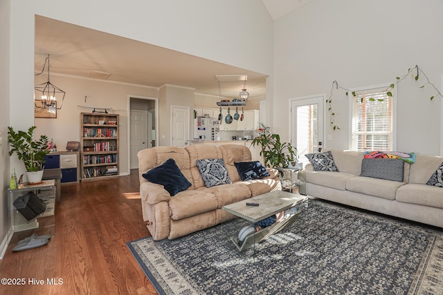 living area featuring ornamental molding, a towering ceiling, wood finished floors, and a chandelier