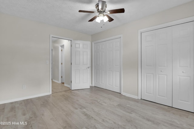 10165 Creekside Dr SE Apt 1, Leland, NC 28451 - unfurnished bedroom with multiple closets, light wood finished floors, baseboards, a textured ceiling, and a ceiling fan