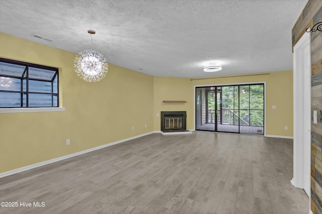 10165 Creekside Dr SE Apt 1, Leland, NC 28451 - unfurnished living room featuring a textured ceiling, a glass covered fireplace, wood finished floors, baseboards, and a chandelier