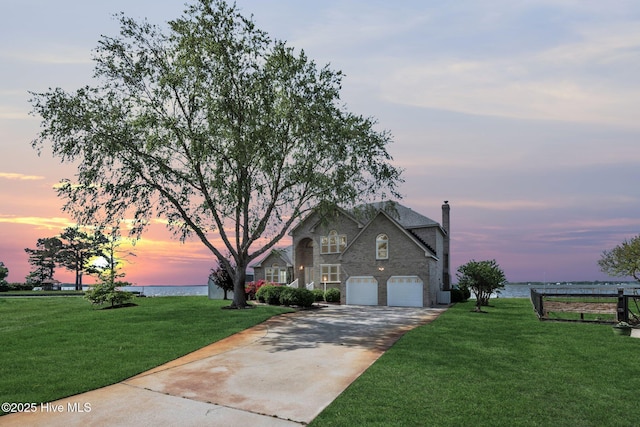 view of front of property with a water view, concrete driveway, a front lawn, and stone siding