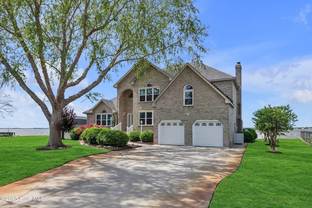 traditional home featuring a front lawn, brick siding, a garage, a chimney, and driveway