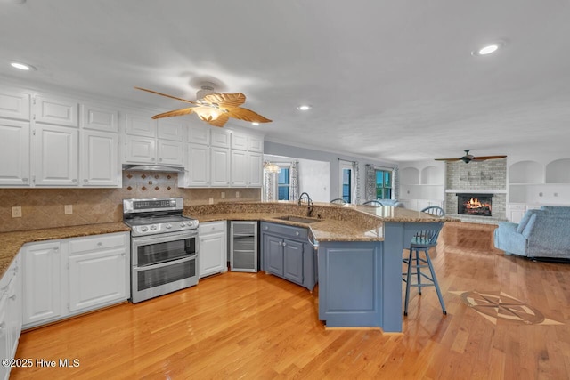 kitchen with a sink, a peninsula, white cabinets, range with two ovens, and a ceiling fan